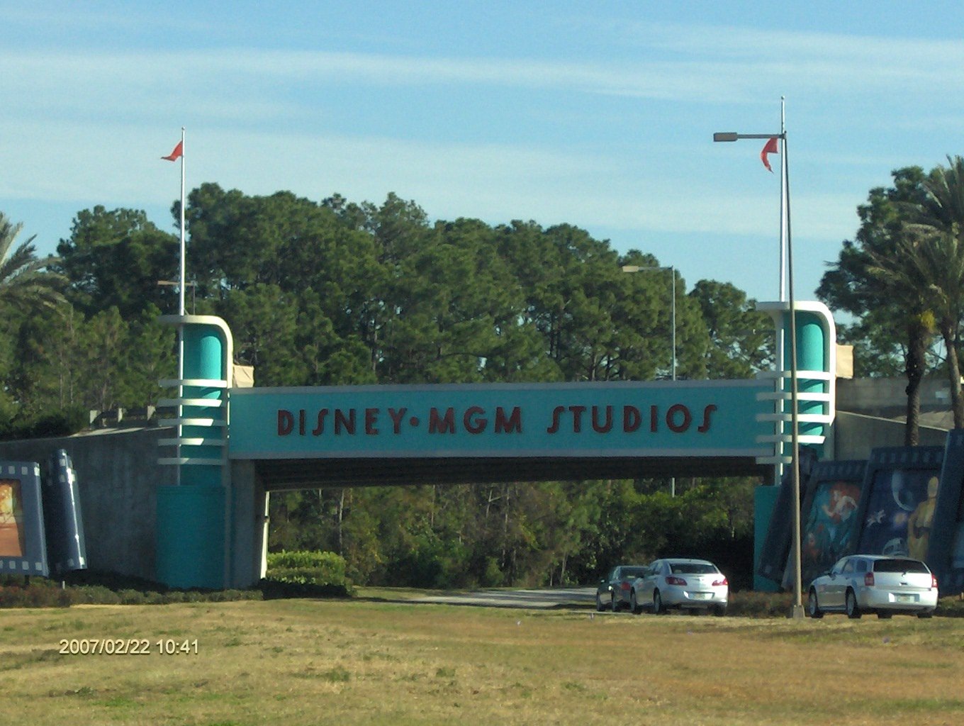 Pórtico de entrada em art déco verde com a inscrição Disney-MGM Studios sobre a estrada
