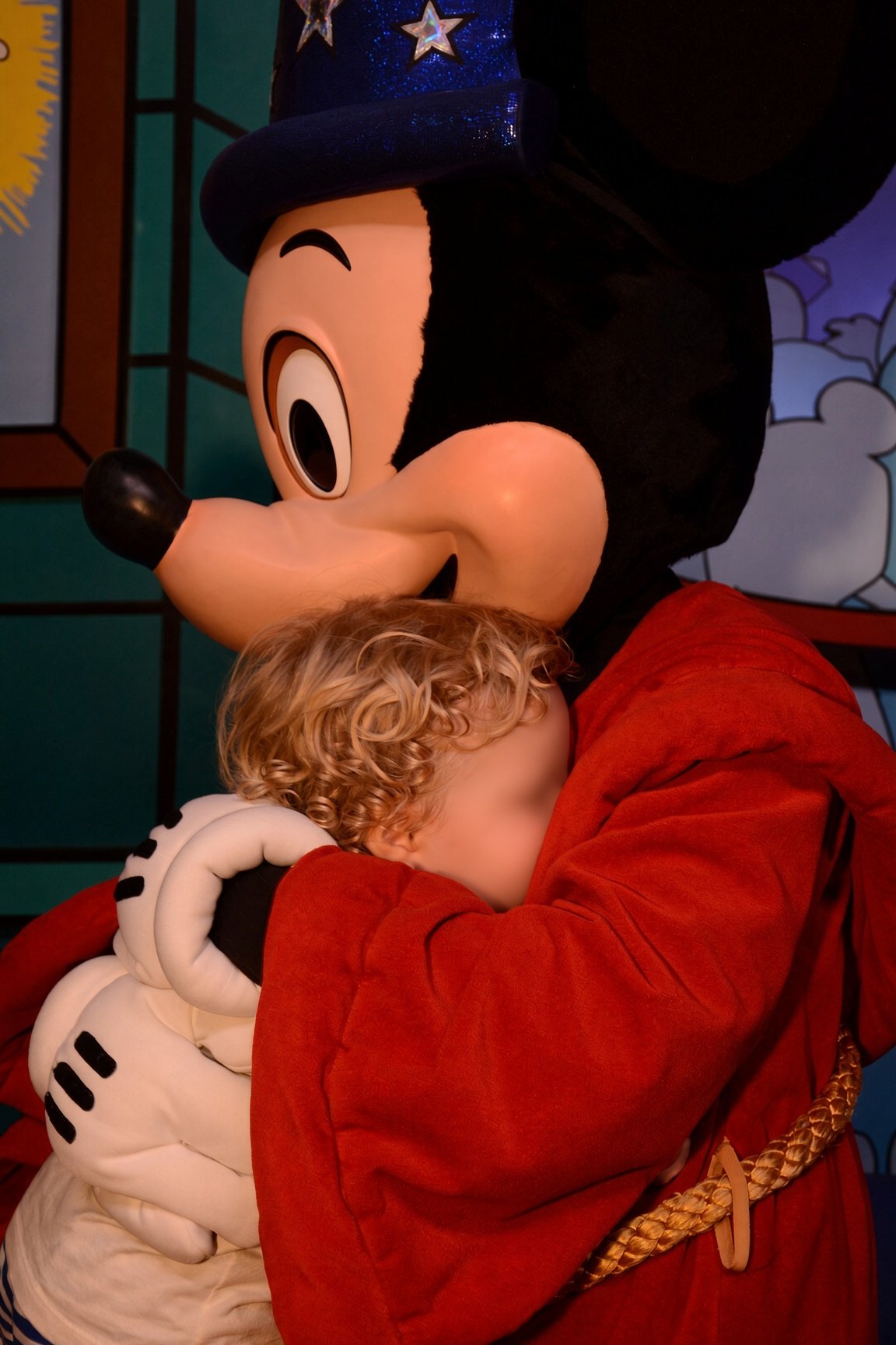 Mickey vestido de feiticeiro abraça uma criança no Hollywood Studios