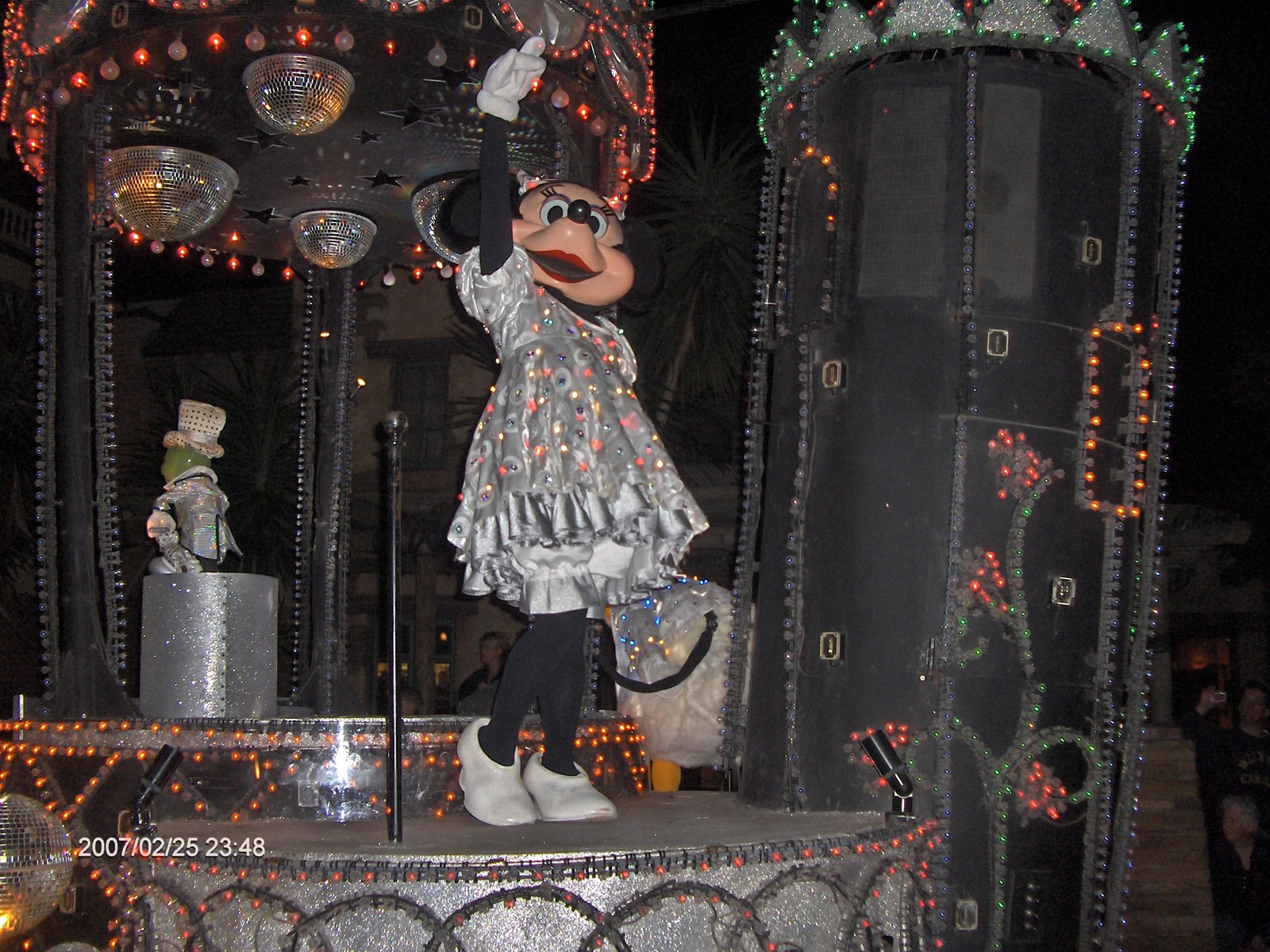 Personagem Minnie em vestido prateado brilhante em cima de carro alegórico iluminado com bolas de discoteca no SpectroMagic