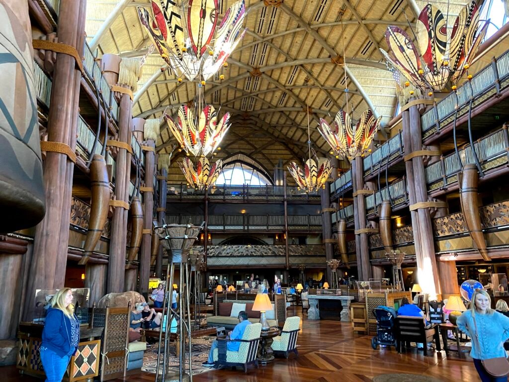 Lobby do Disney's Animal Kingdom Lodge com tematização africana, iluminação natural e altura vertical impressionante